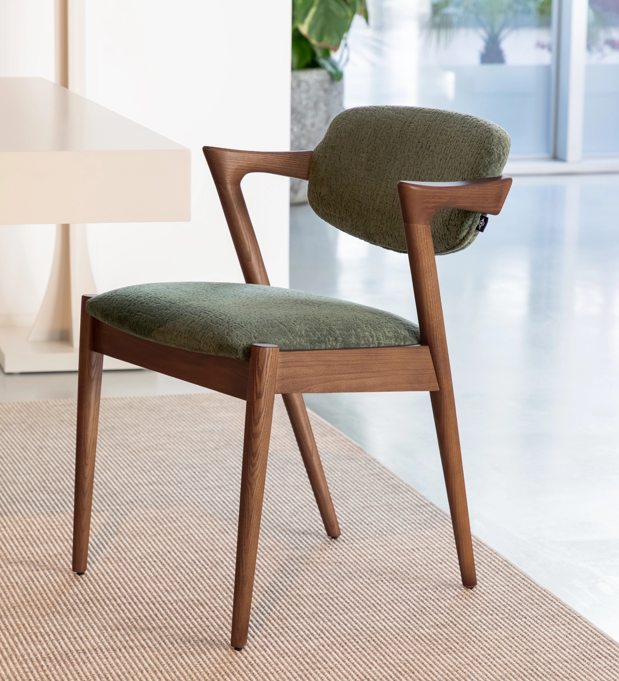 Silla en madera de fresno color nogal, con asiento y respaldo tapizado en tejido verde.