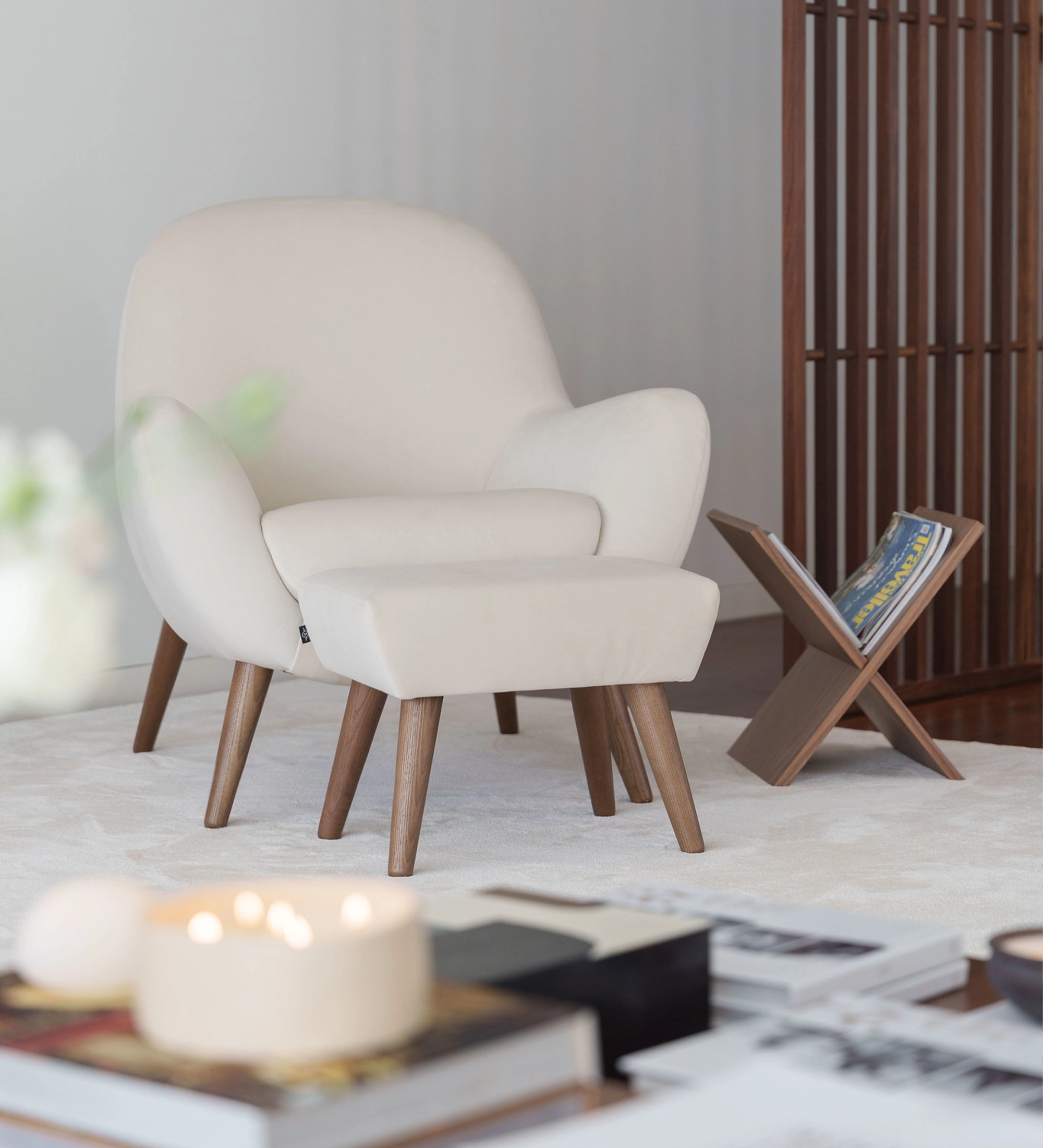 Fauteuil Oslo crème avec repose-pieds et pieds en bois devant baie vitrée