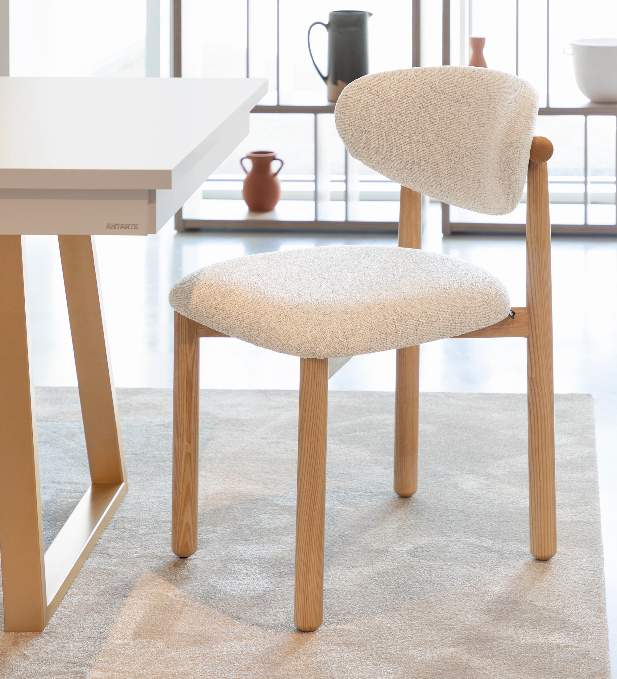 Silla de madera de fresno en color natural, con asiento y respaldo tapizados en tejido perla.