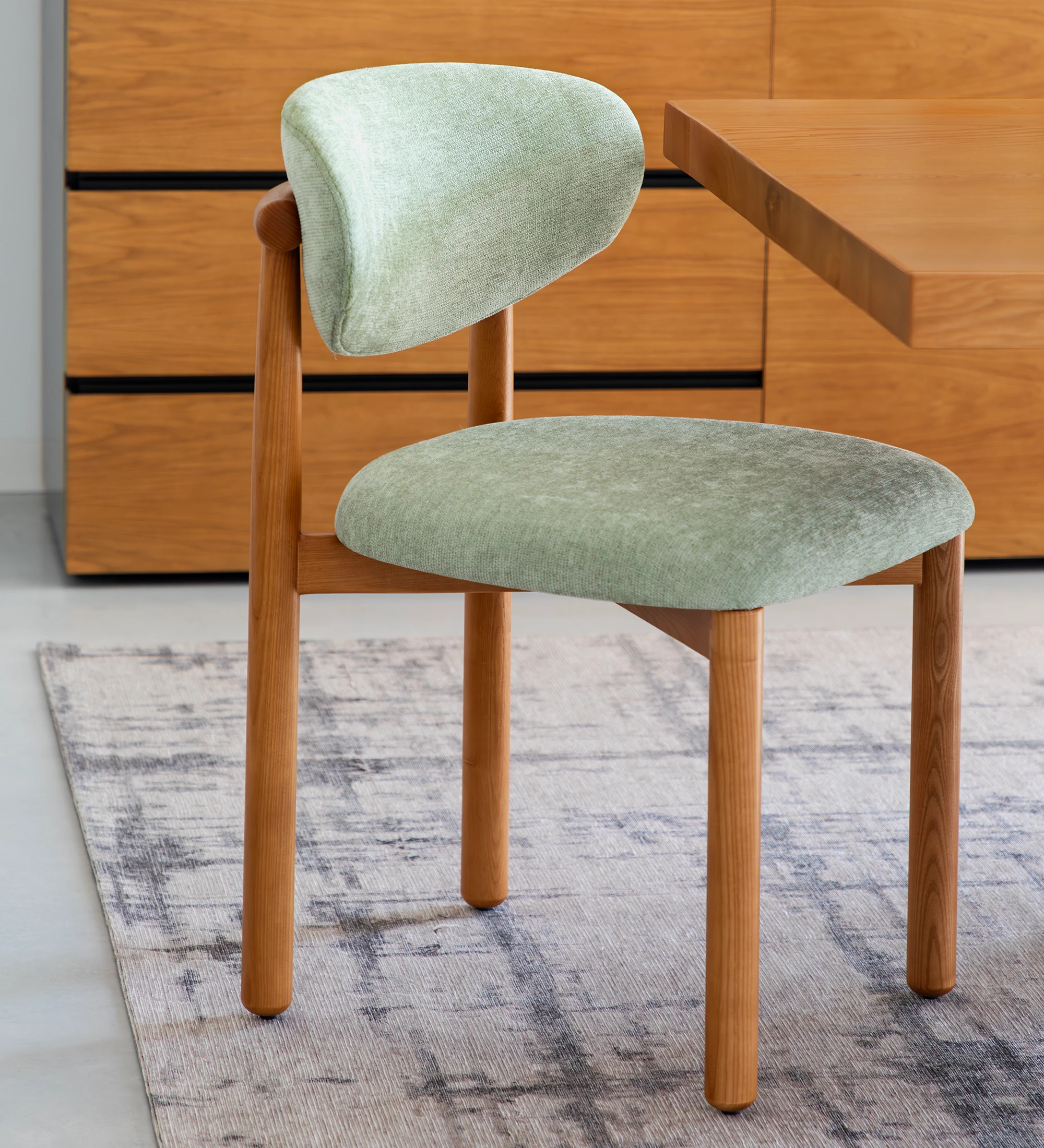 Silla de madera de fresno color miel, con asiento y respaldo tapizados en tela verde.