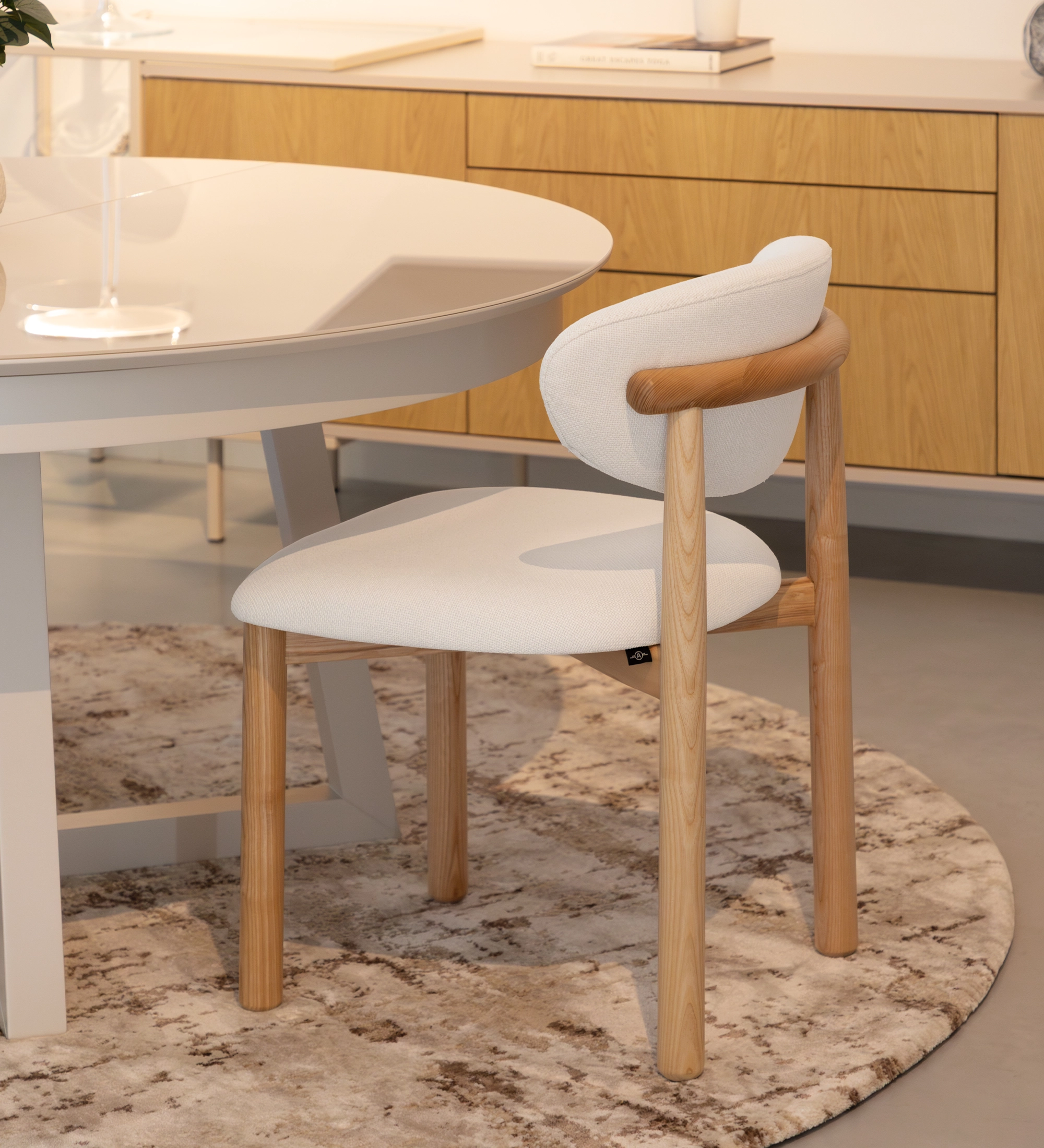 Silla de madera de fresno en color natural, con asiento y respaldo tapizados en tejido blanco.
