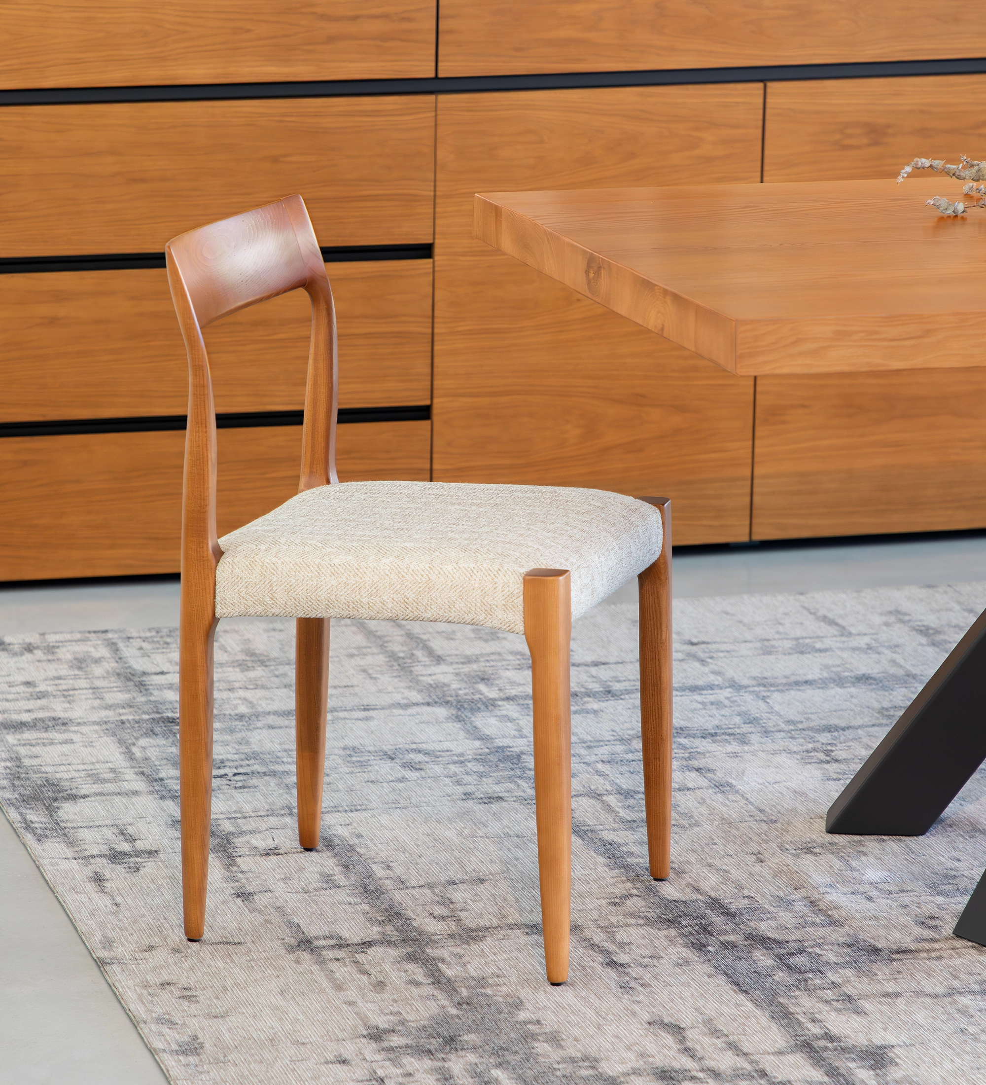 Chair in honey colored ash wood with beige fabric upholstered seat.