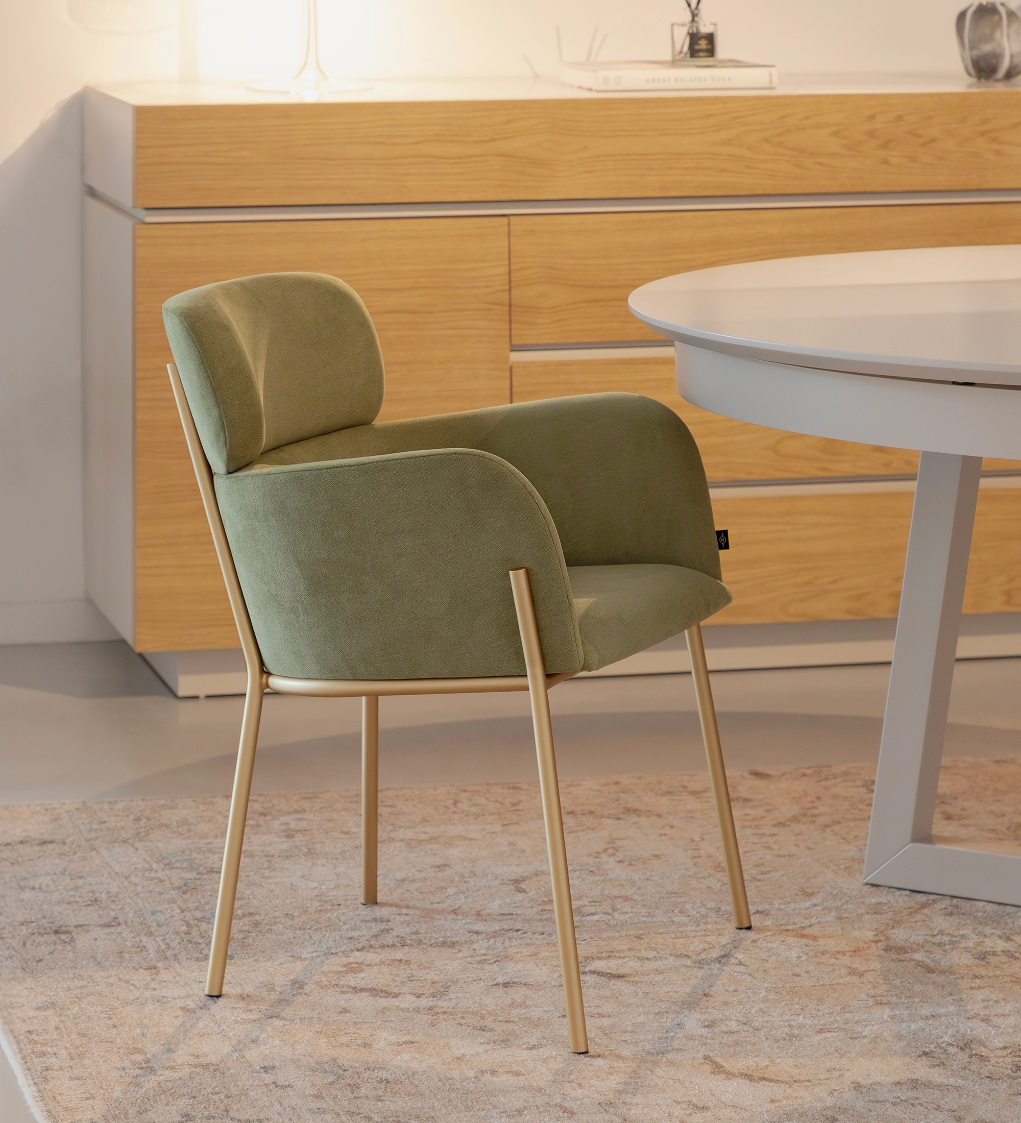 Cadeira Cannes verde estofada com braços e pernas metálicas douradas junto a mesa