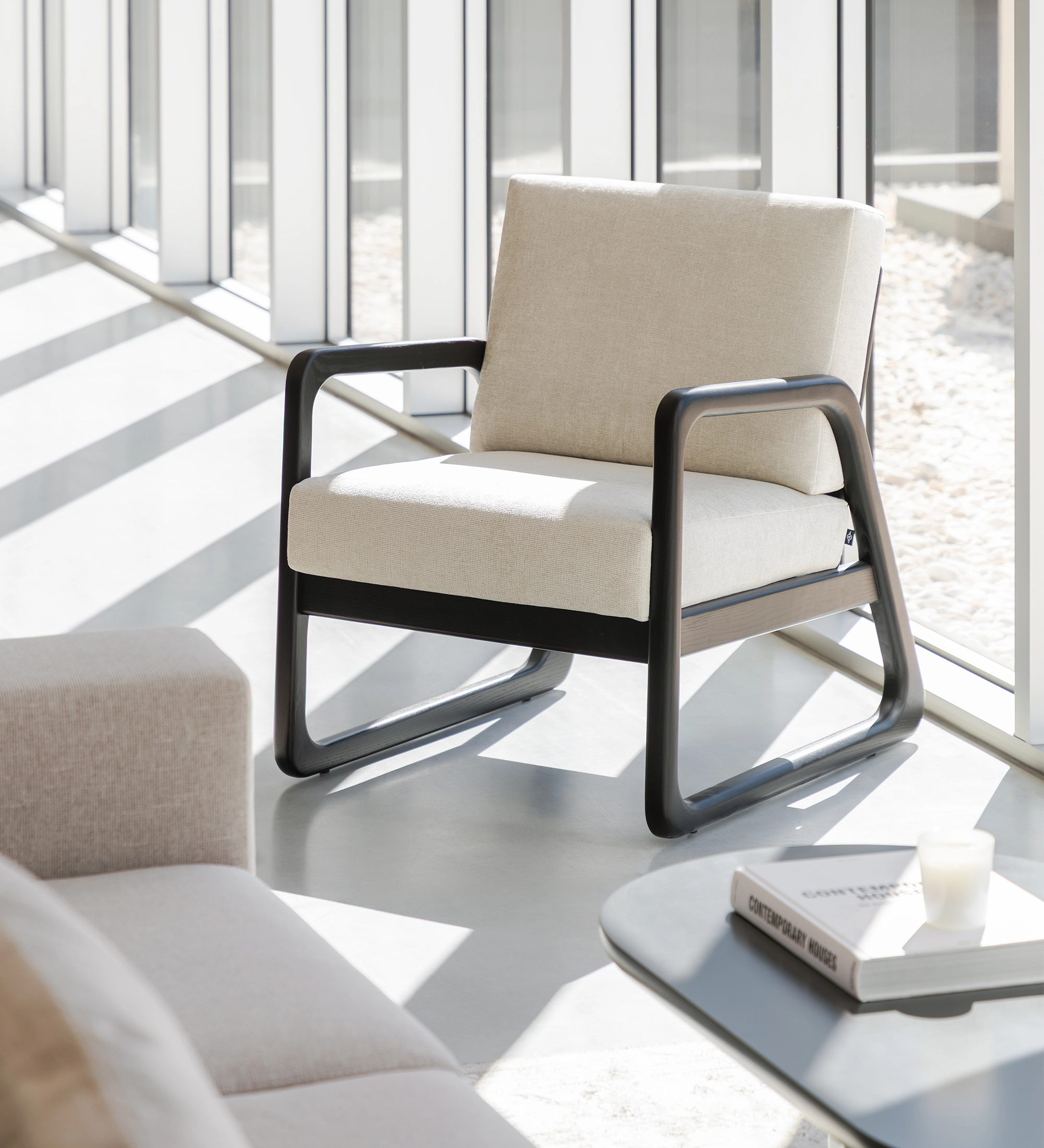Fauteuil Antarte by IA beige, coussins épais et structure noire tubulaire près d'une fenêtre