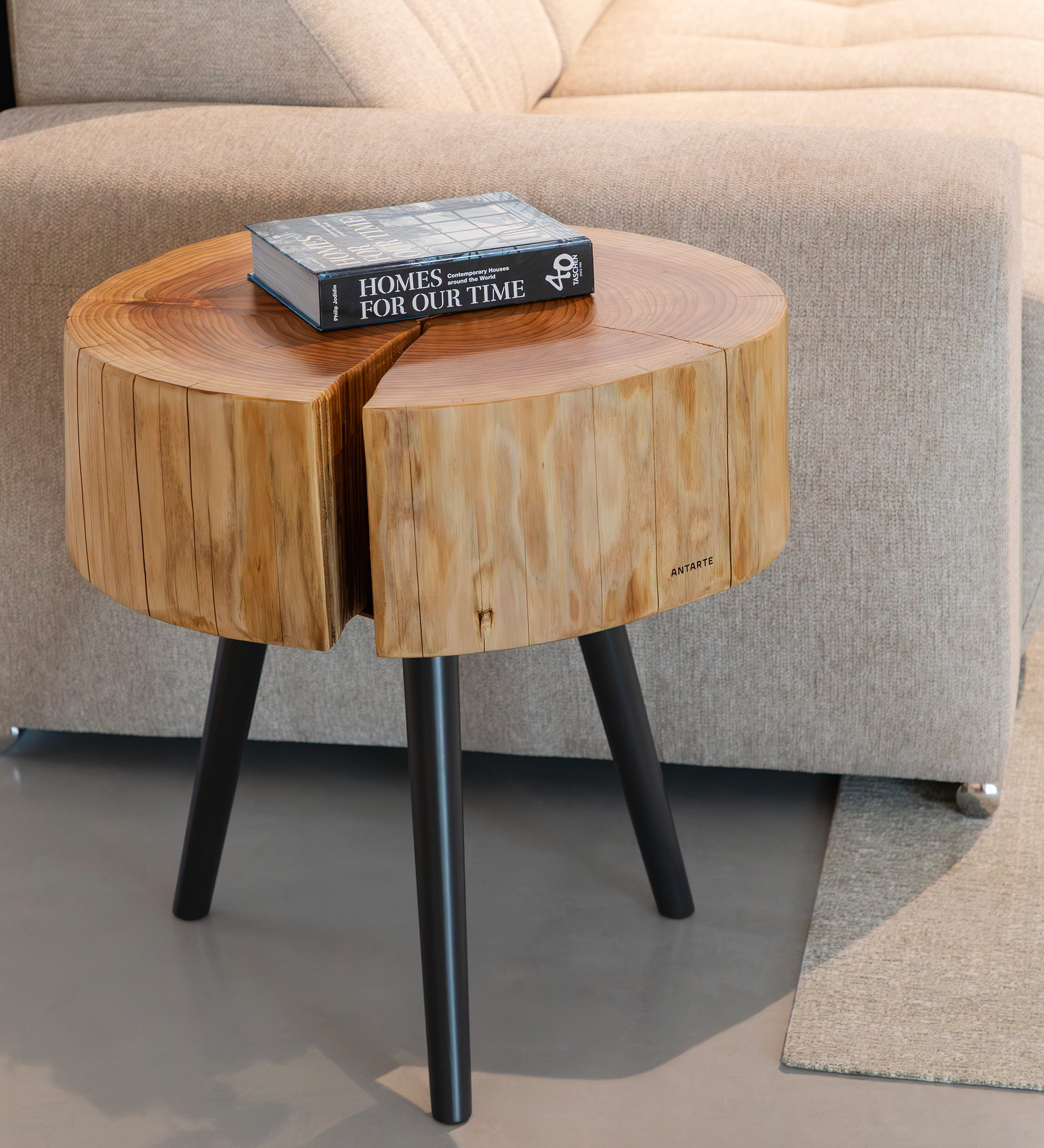 Mesa auxiliar tronco de madera con libro encima y patas negras junto a sofá