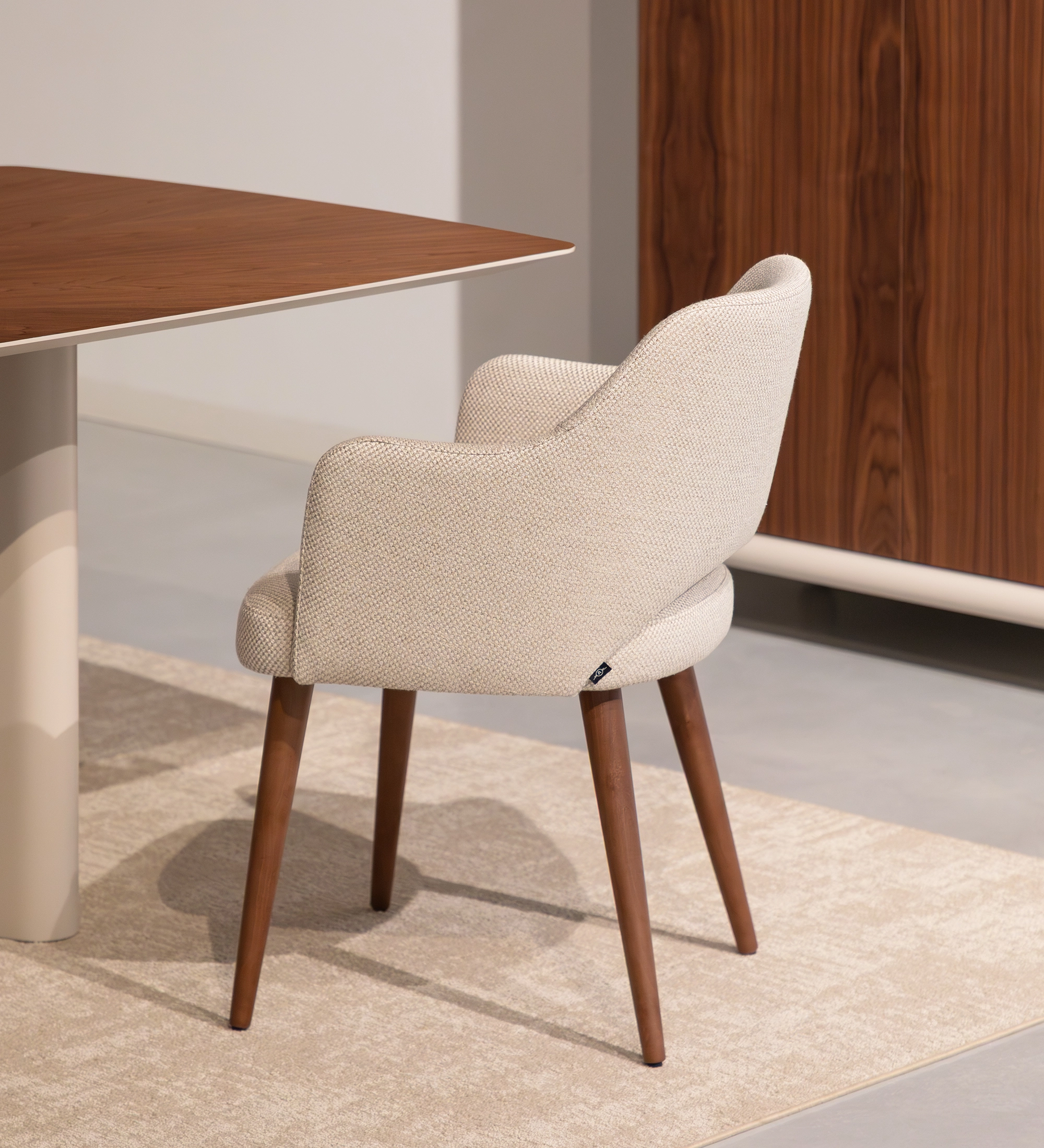 Chaise avec accoudoirs rembourrée de tissu beige et base en bois de noyer.