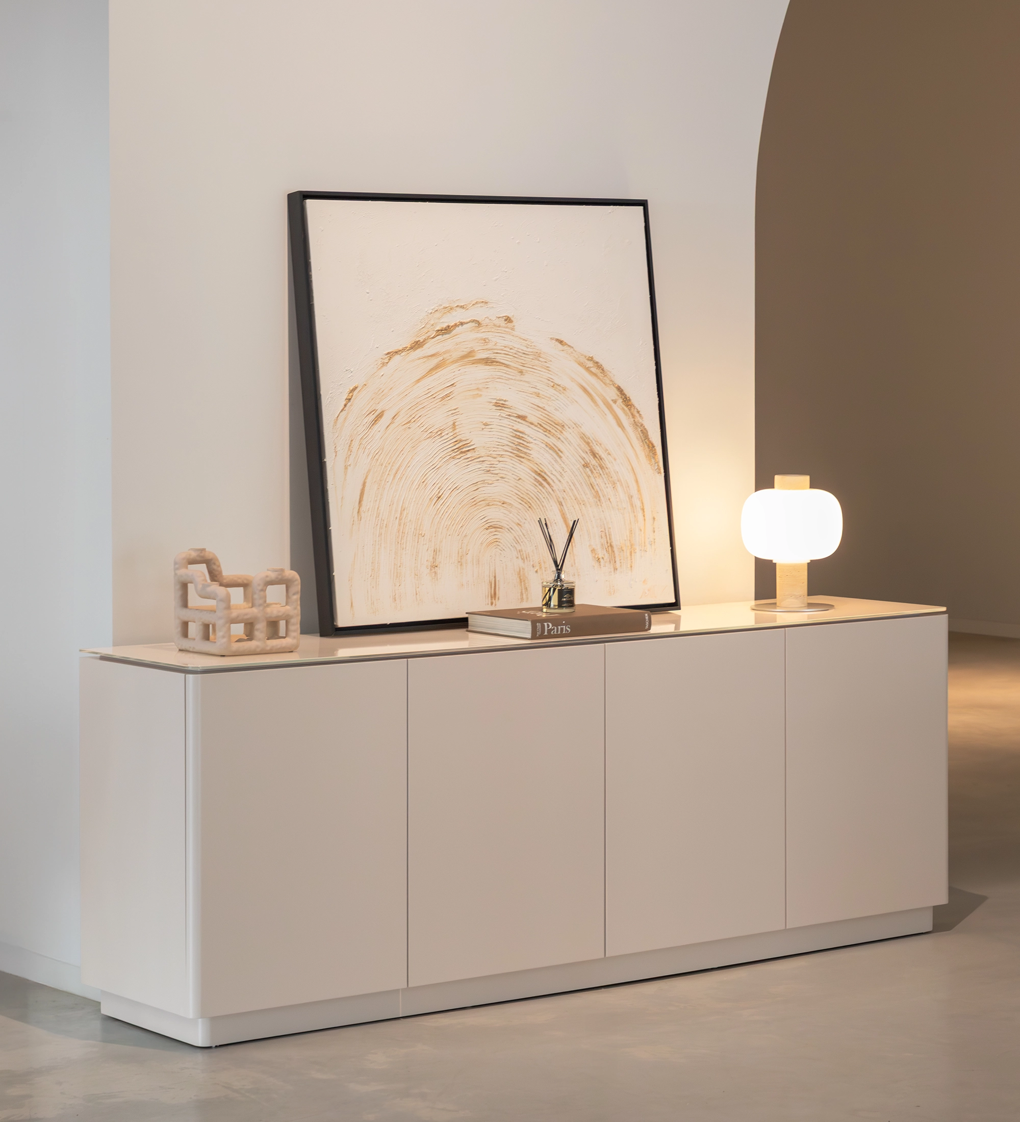 Aparador Geneve blanco con cuadro apoyado, lámpara y objetos decorativos.