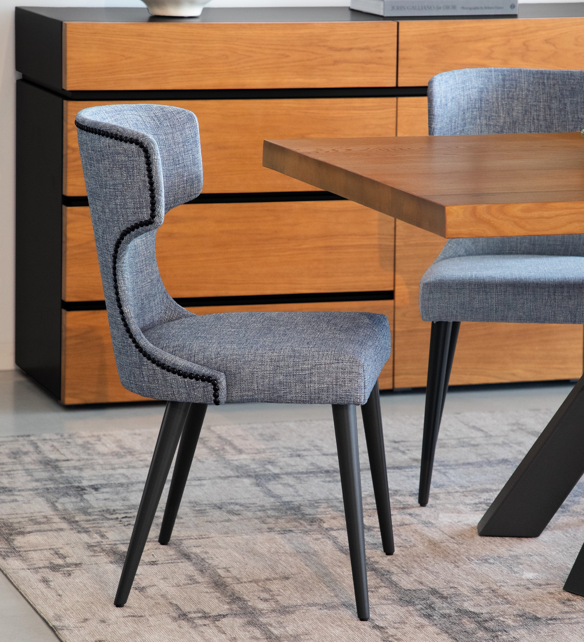 Chaise Pico tissu bleu, pieds noirs, dossier incurvé, près d'une table en bois