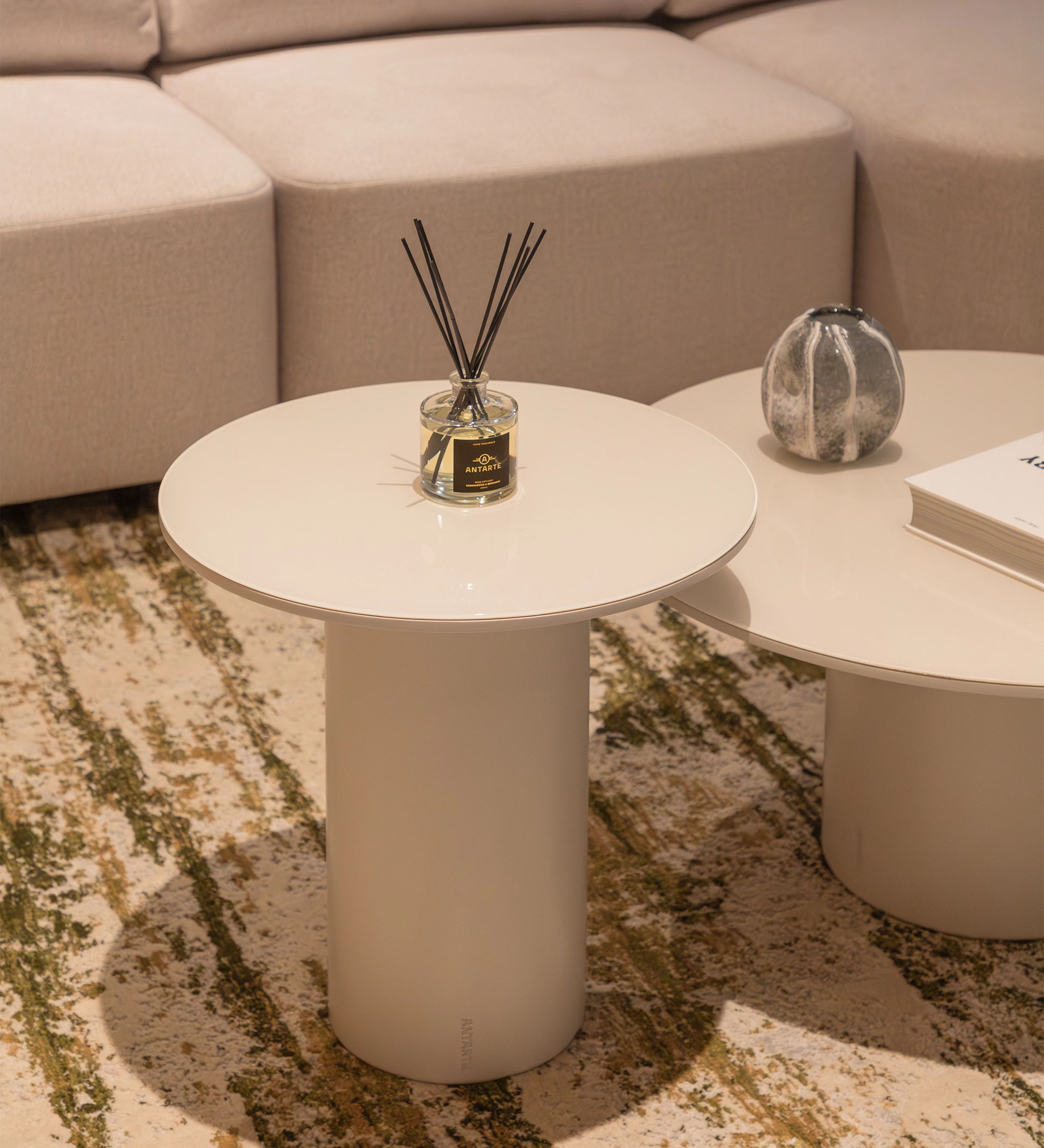 Paris Side Table round cream pedestal with reed diffuser beside beige sofa on patterned rug