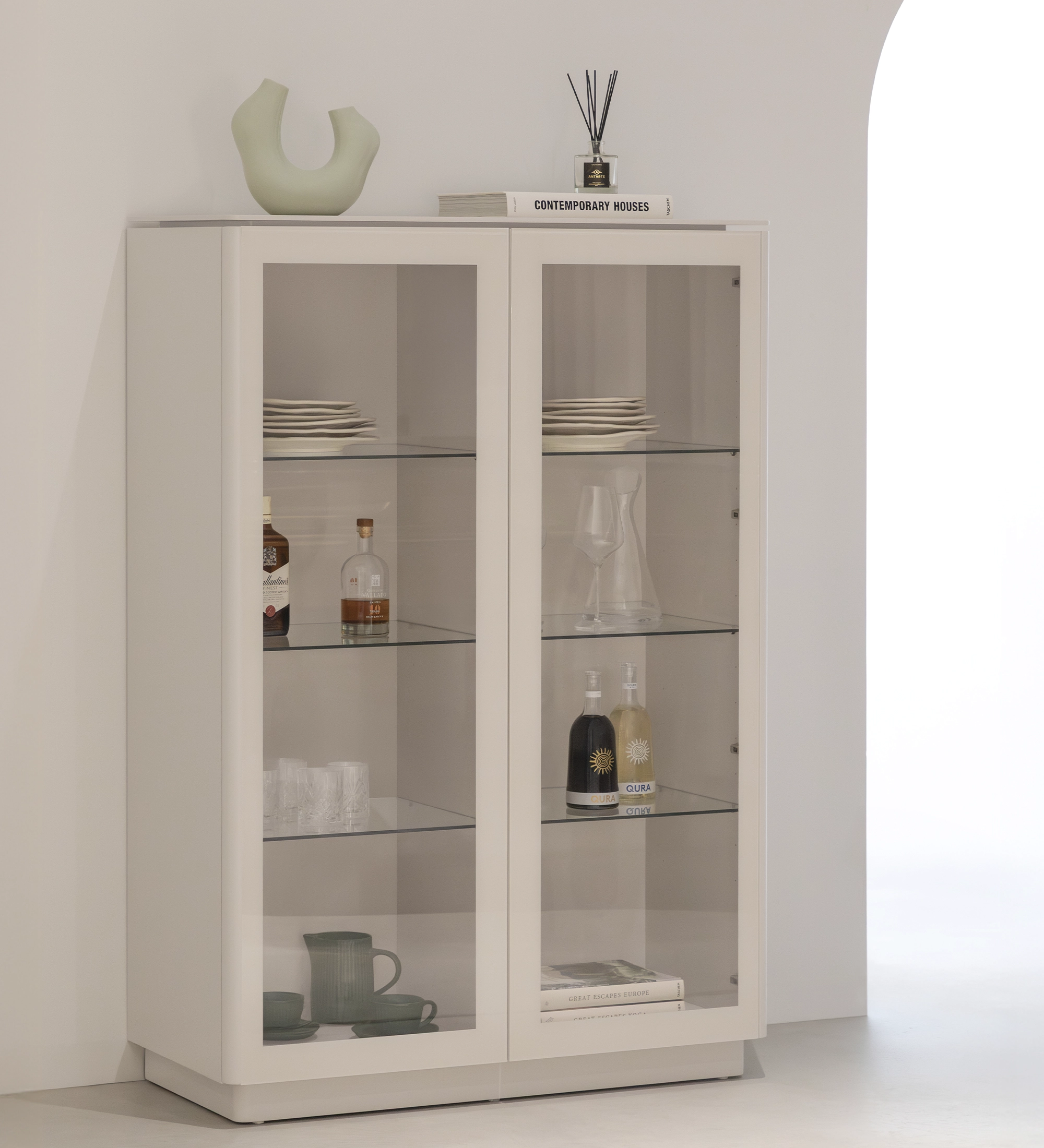 Meuble Vitrine Geneve blanc à portes vitrées avec étagères garnies de vaisselle et bouteilles