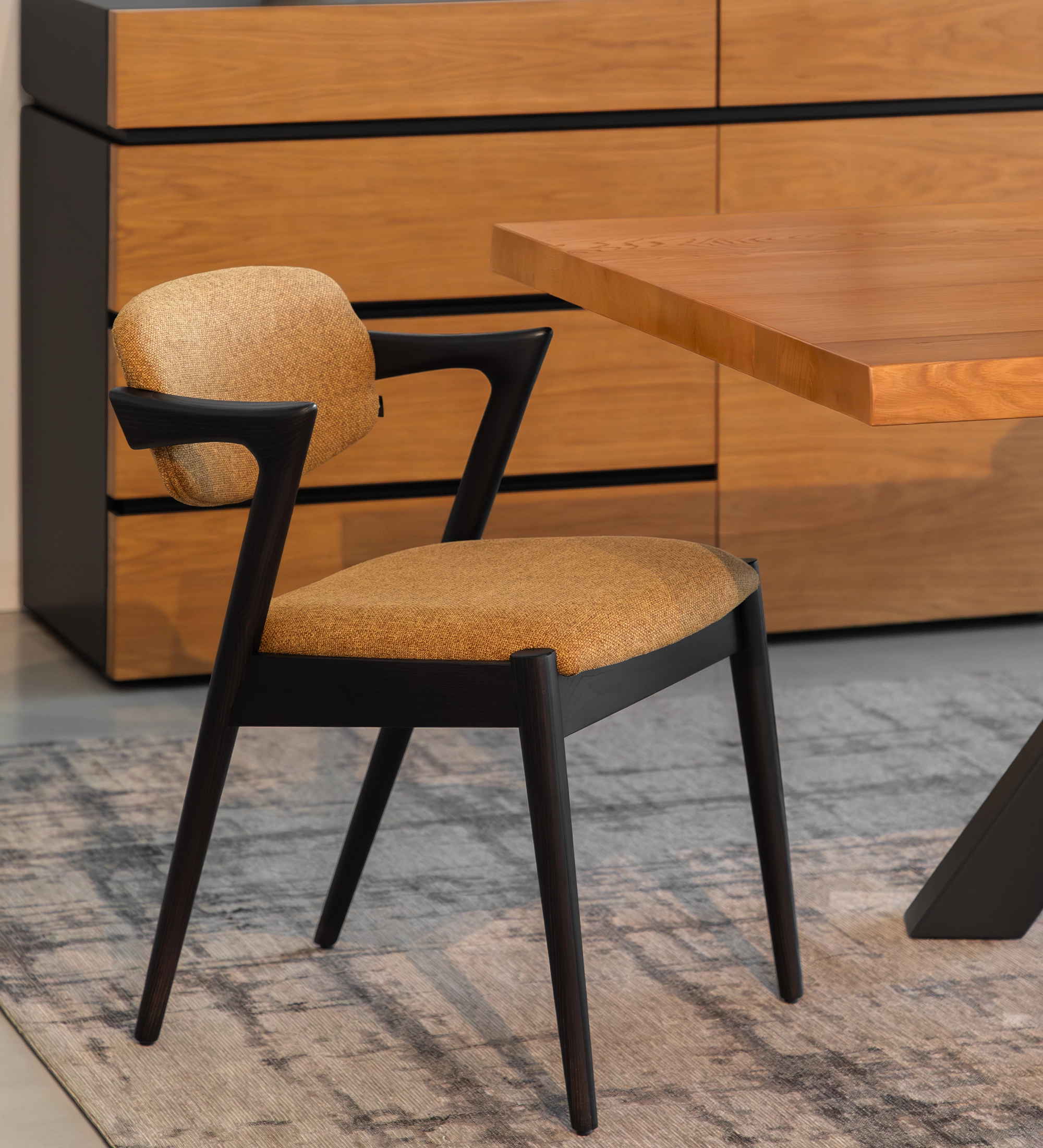 Elba Chair with beige upholstery and black wooden frame beside wooden table