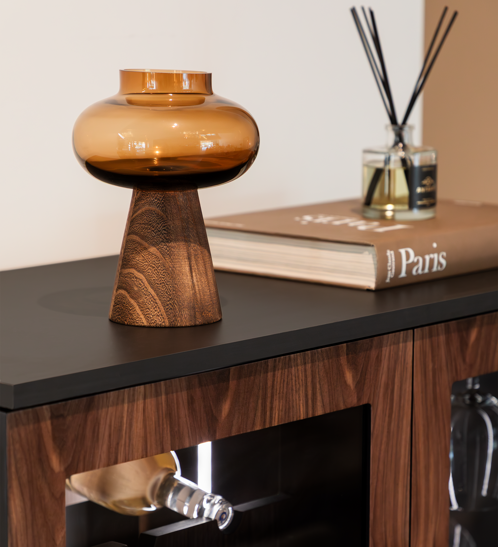 Vinoteca Cannes con lámpara de vidrio ámbar y difusor sobre mueble de madera