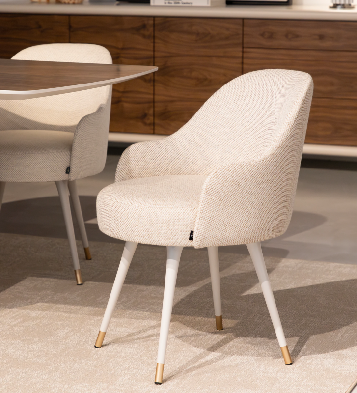 Silla giratoria tapizada en tejido beige, con pies lacados en perla y detalles dorados.