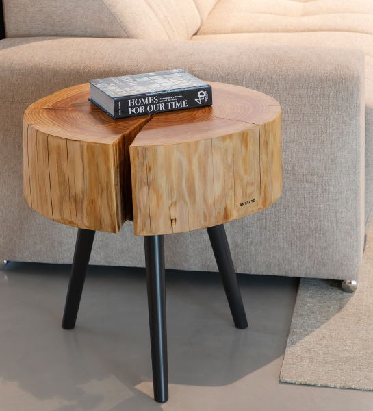 Mesa auxiliar tronco de madera con libro encima y patas negras junto a sofá