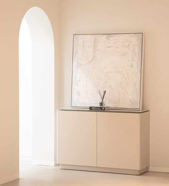 Zapatera Geneve minimalista beige con cuadro y difusor sobre mueble junto a arco