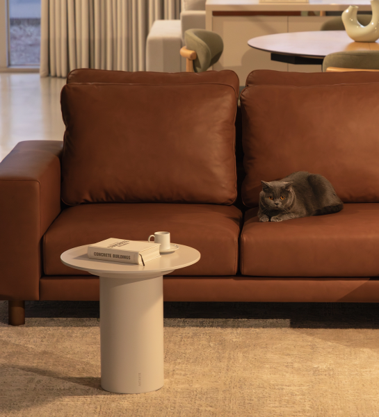 Mesa Auxiliar Paris blanca junto a sofá marrón con libro, taza y un gato gris.