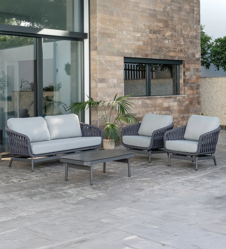 Conjunto de exterior en aluminio antracita, cojines en poliéster gris y tablero de mesa en vidrio cerámico. Respaldo y laterales trenzados en textilene antracita.
