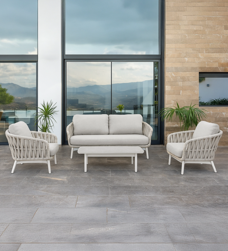 Conjunto de exterior en aluminio blanco, cojines en poliéster gris y tablero de mesa en vidrio cerámico. Respaldo y laterales trenzados en textilene beige.