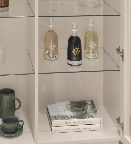 Meuble Vitrine Geneve avec trois bouteilles QURA, tasses vertes et livres