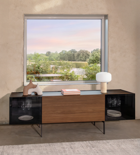 Lagos Sideboard with wooden center, black glass cabinets, lamp and decor under window